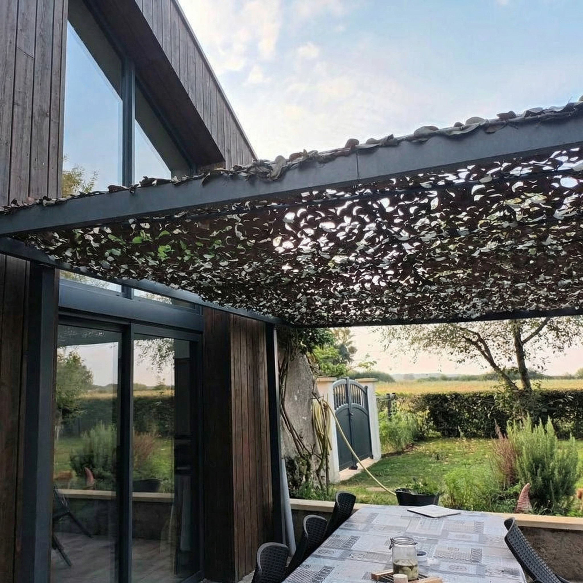 TheFrenchNets woodland print shade net blending into a garden tree line.